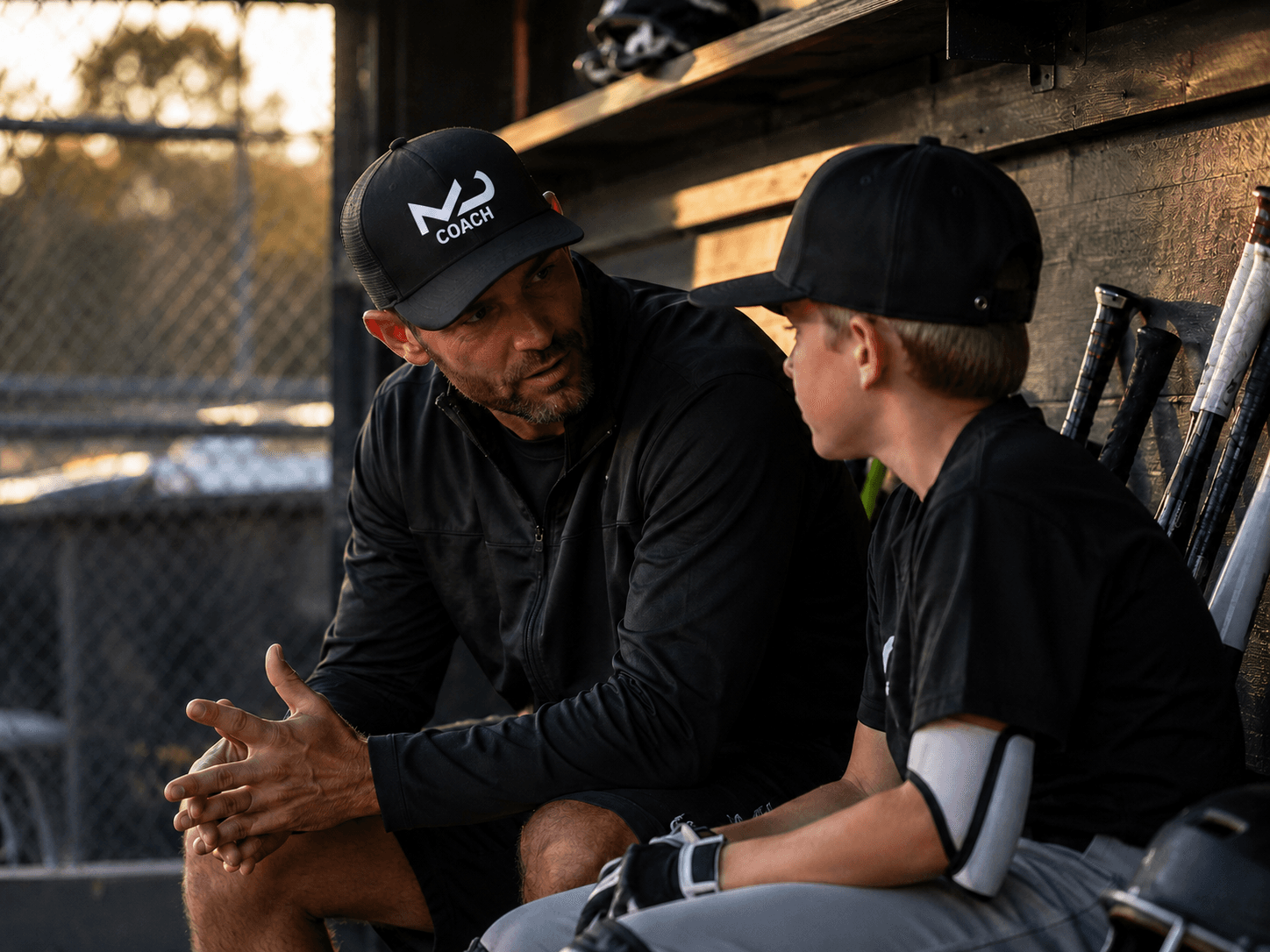 A baseball coach talking with a young player in the dugout.